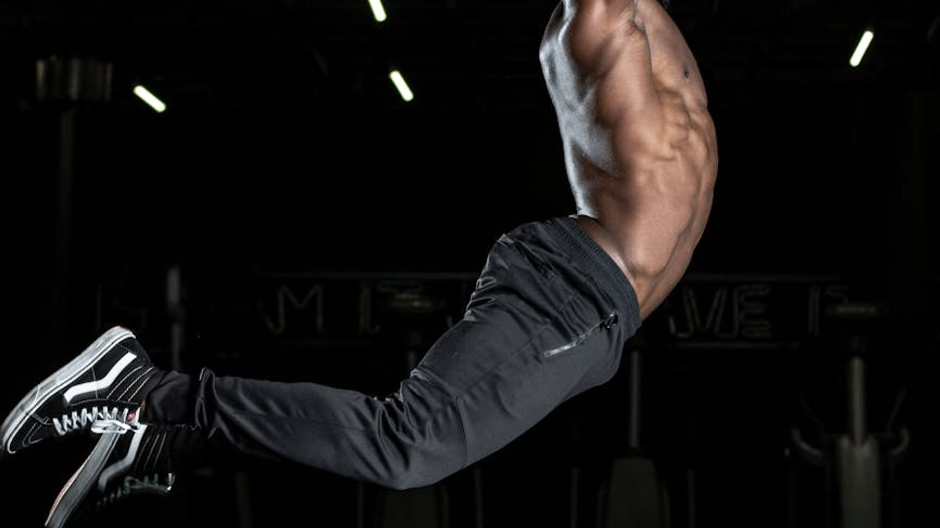 Man performing a controlled strength exercise in a minimalist dark gym.